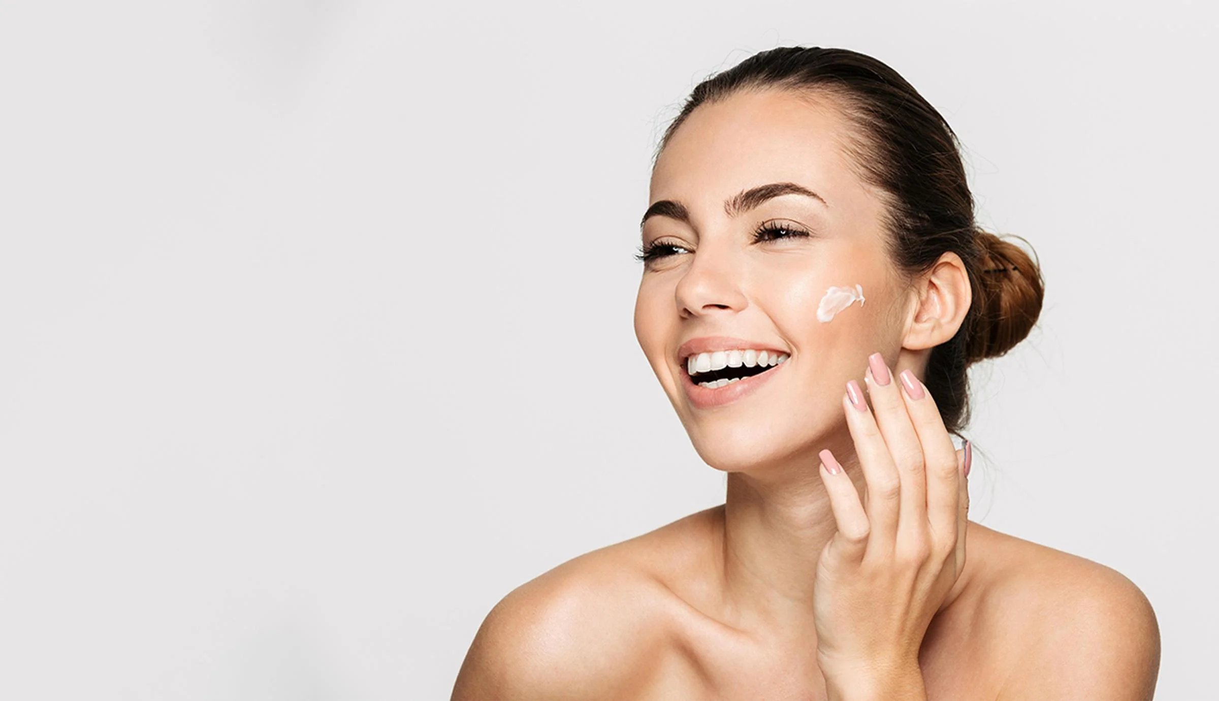 Smiling woman applying skincare cream to her cheek