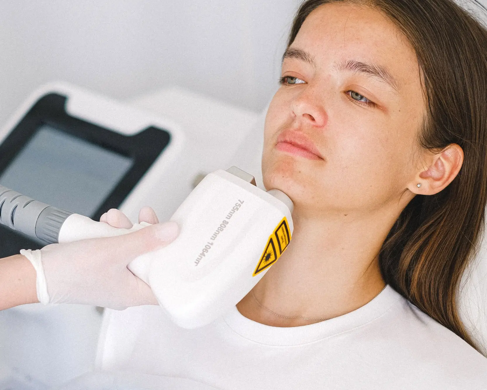 Laser handpiece passing over a patient's jawline during a laser facial