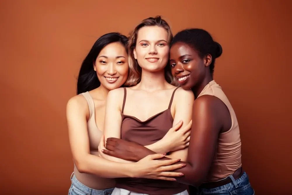 Three women standing together against a warm orange background